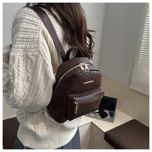 Detail view of brown faux leather backpack with woven texture and gold metal zippers