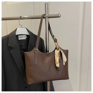 Detail of dark brown leather tote bag featuring adjustable handle and decorative silk scarf