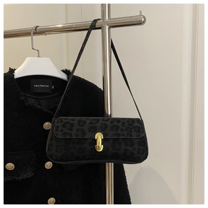 Detail of black leopard print baguette bag with golden buckle on elegant tweed background