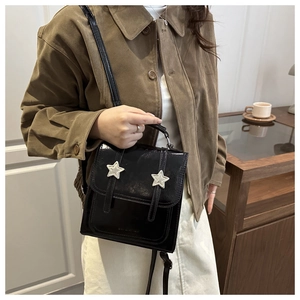 Detail of glossy black faux leather bag featuring silver star patches and hand strap