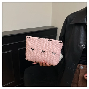 Bolsa de cosméticos rosa acolchada con bordado de lazos negros sostenida en la mano