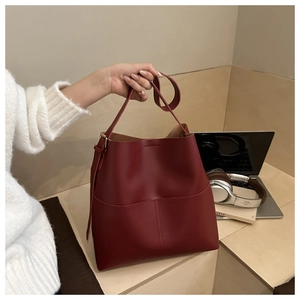 Detail of burgundy leather bucket bag with stitch accents in a modern office setting