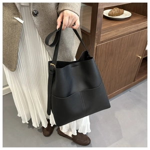 Detail of minimalist black leather bucket bag featuring a front pocket and gold hardware