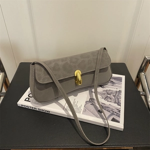 Minimalist grey baguette shoulder bag with golden cylinder lock on an art book