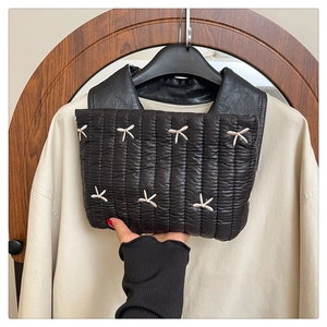 Detalle del bolso acolchado negro con bordado delicado de lazos blancos brillantes