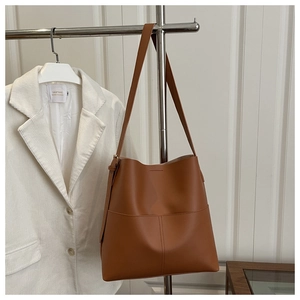 Detail of a brown leather tote bag with vertical stitching on a silver metal stand