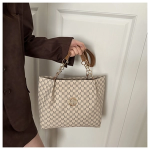 Détail d'un sac cabas avec bandoulière en chaîne dorée et motif M sur fond blanc