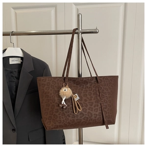 Detailed view of dark leopard print tote bag with plush charm hanging from thin straps