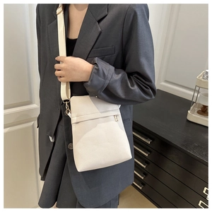 Detail of white lychee textured leather crossbody bag with wide strap on grey suit