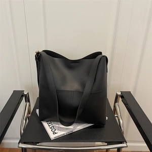 Minimalist large capacity black bucket tote bag displayed on a modern leather chair
