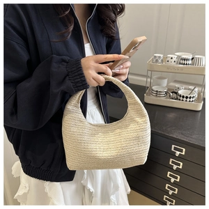 Détail du sac à main tissé beige en forme de croissant porté avec une veste marine