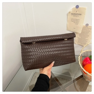 Detail of dark brown woven leather clutch bag with elegant gold-tone hardware clasp
