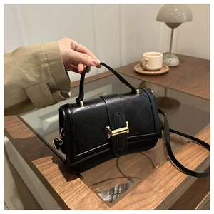 Détail d'un sac bandoulière matelassé noir avec boucle dorée et poignée en cuir