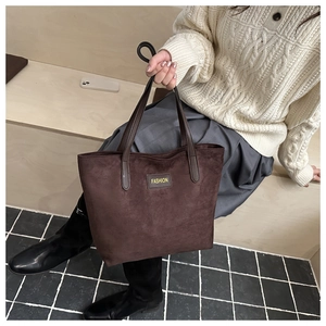 Detail einer braunen Wildleder-Tragetasche mit 'FASHION'-Label und doppelten Schultergurten
