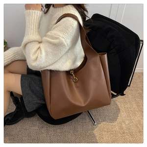 Close-up of brown leather tote bag with gold metal buckle detail on white knit top