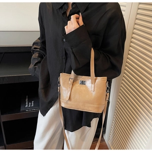 Détail du sac seau beige avec fermoir en métal et bandoulière dans une pièce