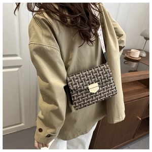 Close-up of a tweed crossbody bag featuring a metal shield lock and embroidered wide strap