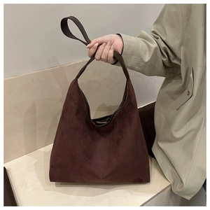 Detail of dark brown suede hobo tote bag held by a model in a khaki trench coat