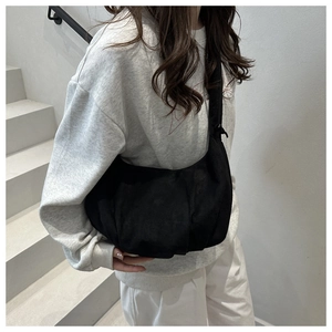 Modèle portant un sac hobo noir plissé mat sur l'épaule dans un décor minimaliste