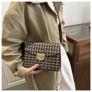 Detail of tweed crossbody bag with golden shield buckle worn with khaki trench coat