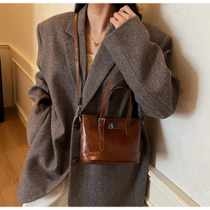 Détail d'un sac bandoulière marron brillant avec fermoir argenté sur une tenue chic
