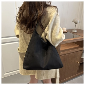 Minimalist black large capacity shoulder bag shown on a model in a cozy interior setting