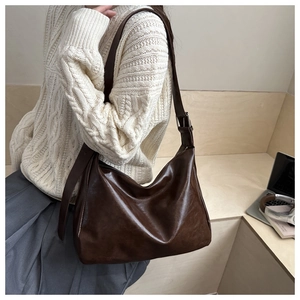 Detail of dark brown wax leather bag showing texture, wide strap, and metal buckle