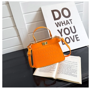 Primer plano del cuero naranja con grabado de cocodrilo y cierre giratorio dorado del bolso