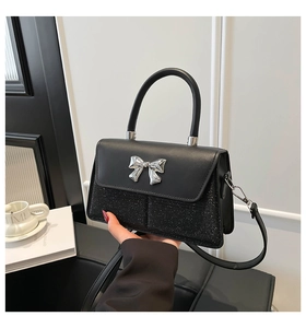 Detail of the black crossbody bag showing matte leather and glitter texture with silver bow