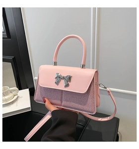 Detailed shot of pink crossbody bag featuring a metallic bow buckle and sequined texture