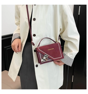 Close-up of burgundy leather crossbody bag with white stitching and gold lock detail