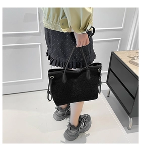 Detail of large black plush tote bag with slim leather handles in a chic indoor setting