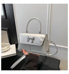 Detail of silver crossbody bag with a metallic bow clasp and sparkling fabric texture