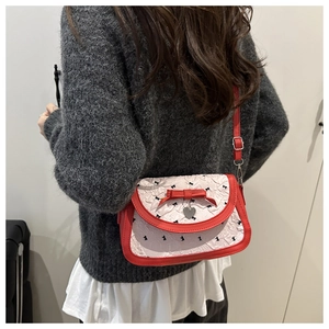 Détail du sac à nœud rouge et blanc avec pendentif cœur sur un pull en maille gris