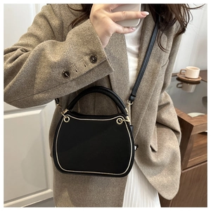 Detail of a chic black semi-circle handbag with golden hardware worn on a brown blazer