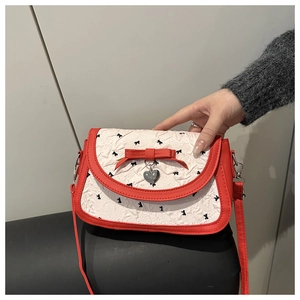 Détail du sac matelassé rouge et blanc avec motif nœud, pendentif cœur et bandoulière rouge