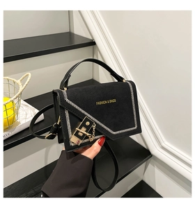Detailed view of the black suede textured handbag featuring a gold lock and chain strap