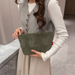 Detail of dark green corduroy envelope clutch featuring a red fashion label on the side