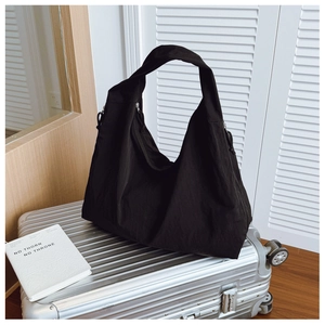 Macro detail of high-capacity black nylon hobo tote bag with wide strap on silver suitcase
