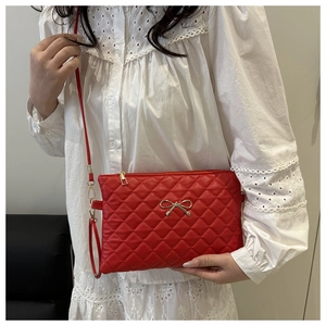 Détail du sac bandoulière matelassé rouge avec nœud doré décoratif et fermeture éclair