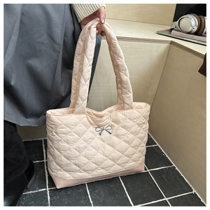 Detail of light pink quilted tote bag featuring a silver metallic bow and puffer texture