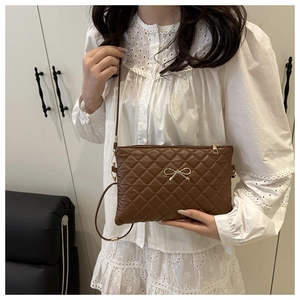 Detail of brown quilted crossbody bag with golden bow and metal zipper closure