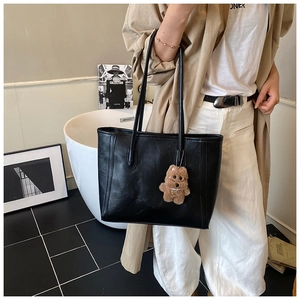 Detail of black faux leather tote bag with long straps and brown plush bear charm accessory