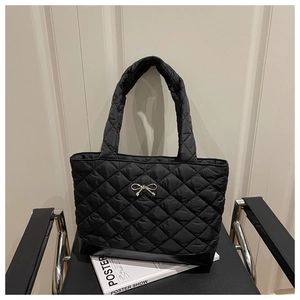 Detailed view of black quilted tote bag with silver bow ornament and chic metal texture