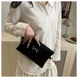 Close-up of black quilted shoulder bag with elegant gold metal bow and luxe finish