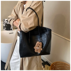 Detail of a black leather tote bag with a cute brown bear charm on the shoulder strap