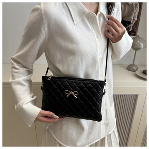 Detail of black quilted shoulder bag with elegant gold metal bow clasp and leather strap