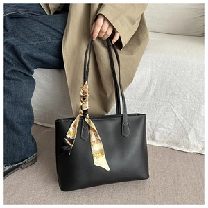 Detail of black tote bag with white contrast stitching and a silk scarf on handle