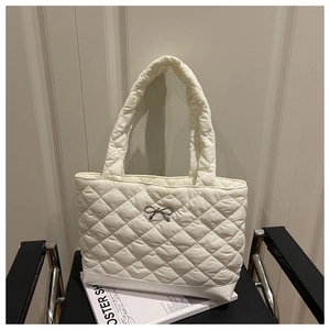 Close-up of white quilted tote bag with silver bow detail on a black metal chair