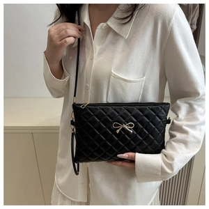 Close-up of black quilted shoulder bag with gold bow clasp and glossy PU leather
